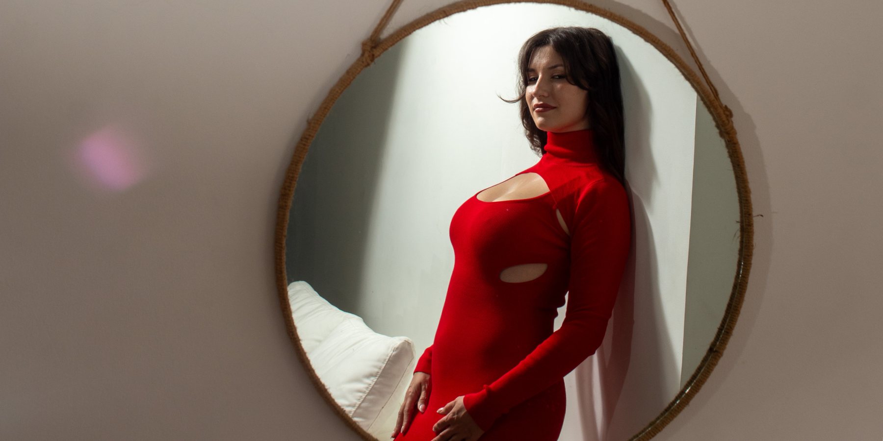 Sophia Lee Fox in a red dress, reflected in a round rope-hung mirror against a soft grey wall