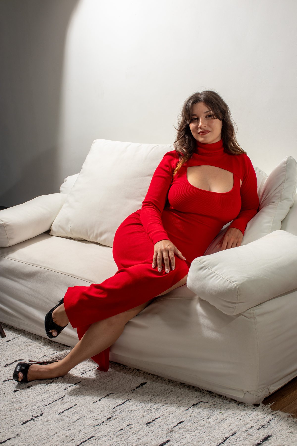 Sophia Lee Fox, founder of Saha Synergy, seated on a white sofa in a red dress and looking toward the camera